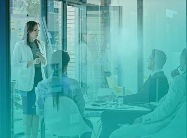 Executive presenting to a leadership team in a glass-walled conference room during a management due diligence review