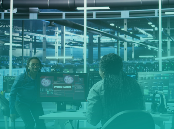 Two team members in a control room react to a “System hacked” warning on a monitor, with a large industrial facility visible through the windows.