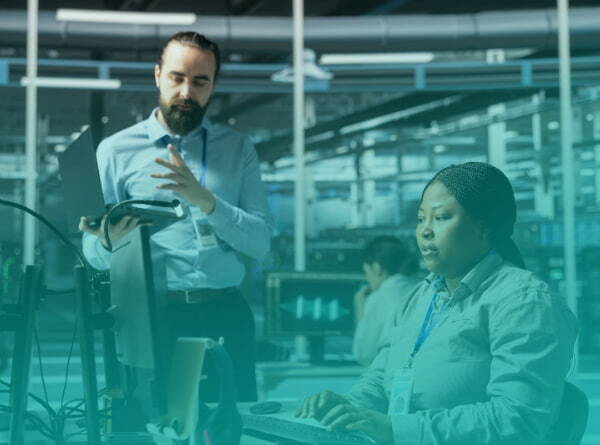 Two engineers reviewing production data at workstations inside a manufacturing facility